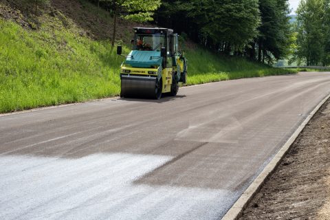 Straßenbauarbeiten mit Verdichtungsmaschine auf neu asphaltierter Straße.
