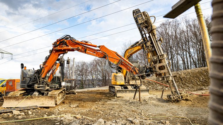 Bauarbeiten mit Bagger und Bohrgerät auf einer Baustelle.