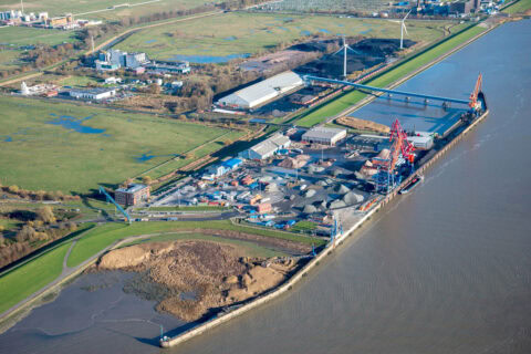 Hafen mit Kränen, Lagerflächen und Wasserbauarbeiten an der Küste.