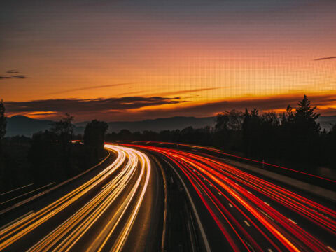 Blick auf eine Autobahn bei Sonnenuntergang mit Lichtspuren der Fahrzeuge.
