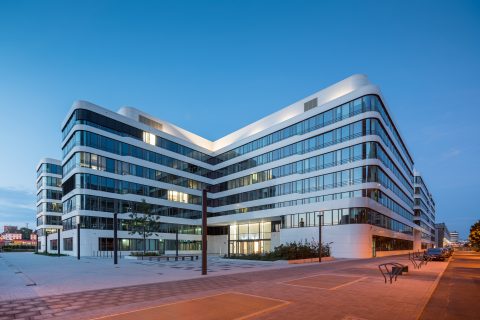 Modernes Bürogebäude bei Dämmerung, beleuchtete Fassaden.