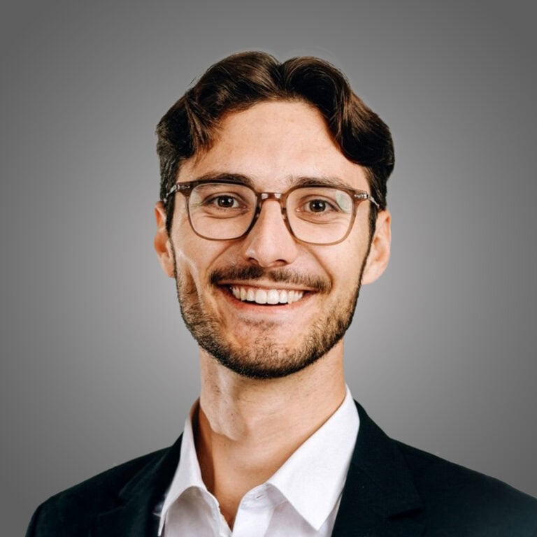 Freundlicher junger Mann in Businesskleidung vor grauem Hintergrund.