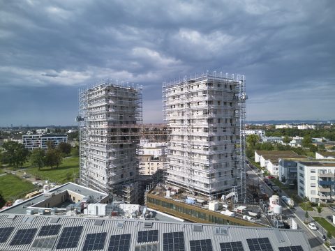 Zwei im Bau befindliche Hochhäuser mit Gerüsten in einer Stadt.