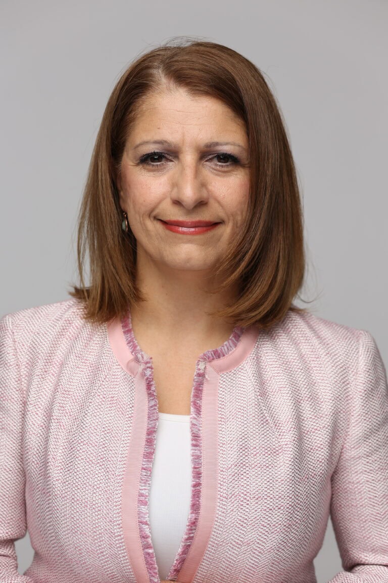 Frau in professioneller Kleidung vor neutralem Hintergrund.