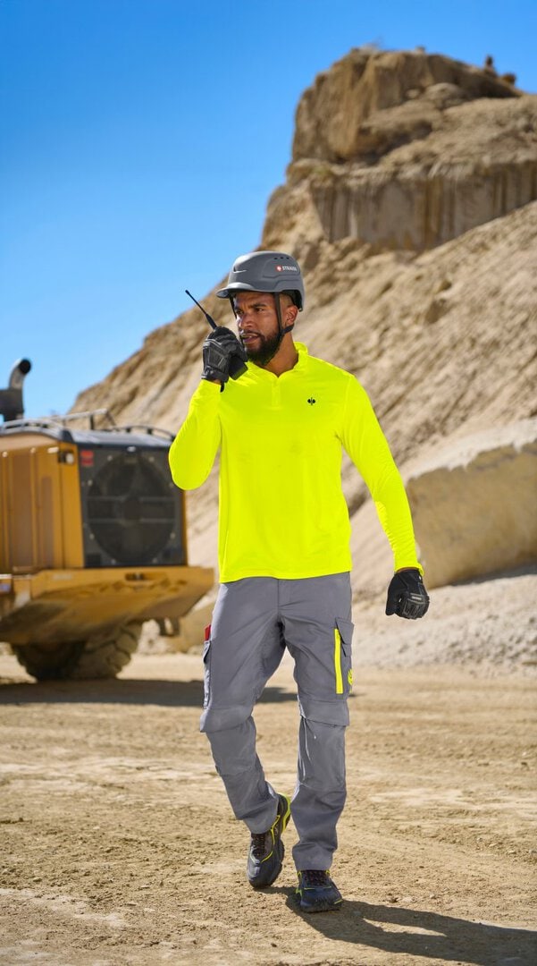 Mann auf Baustelle trägt helle Jacke und spricht ins Funkgerät.