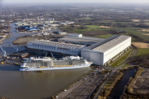 Großes Lager- und Produktionsgebäude am Wasser mit Kreuzfahrtschiff im Hafe.