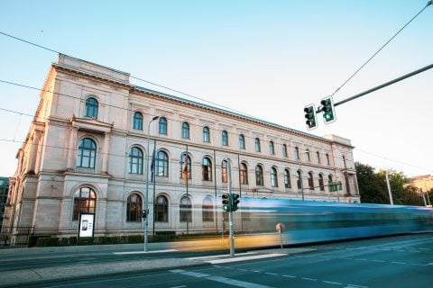 Historisches Gebäude am urbanen Straßenrand mit Verkehrsampeln und Tram.