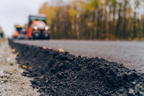 Straßenbauarbeiten auf einer Landstraße, mit Baumaschine im Hintergrund.